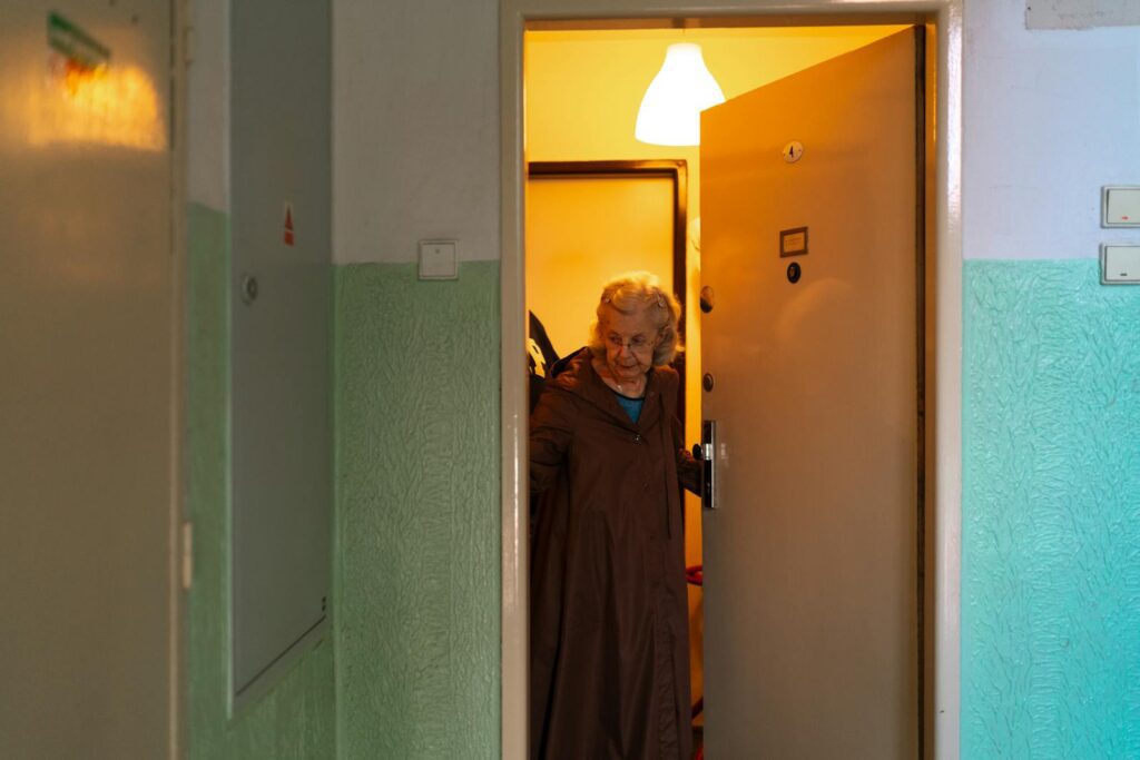 Senior woman opening her door, depicting home life and independence in Praha.