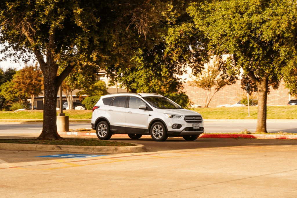 White SUV parked under shady trees in a sunny parking lot during fall.