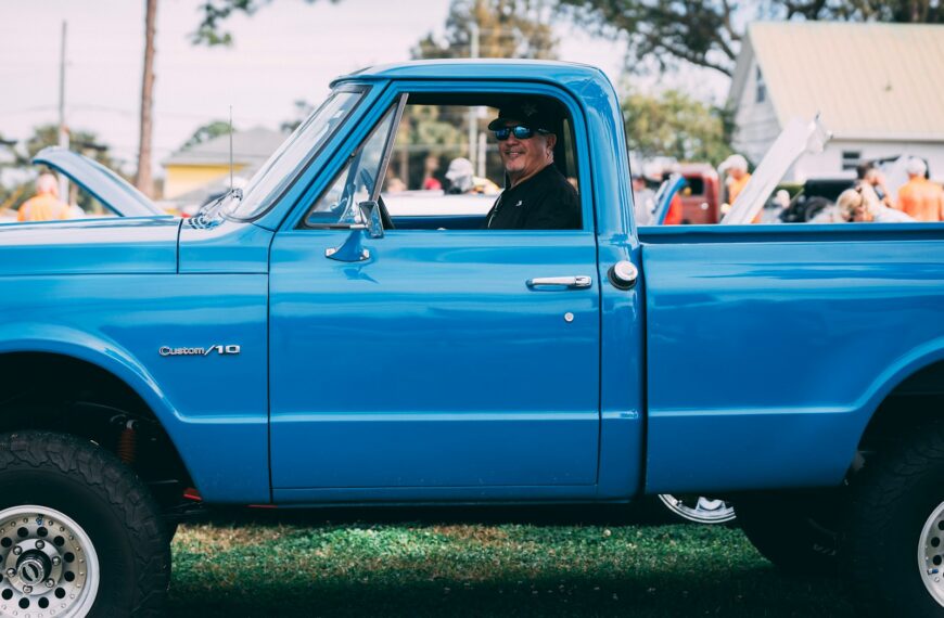 Man in sunglasses driving a bright blue pickup truck.