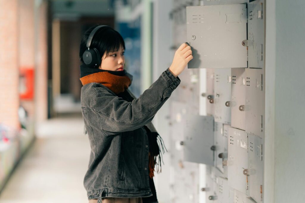 Asian woman in scarf and headphones checking mailbox in a corridor. Indoor urban setting in Hanoi, Vietnam.