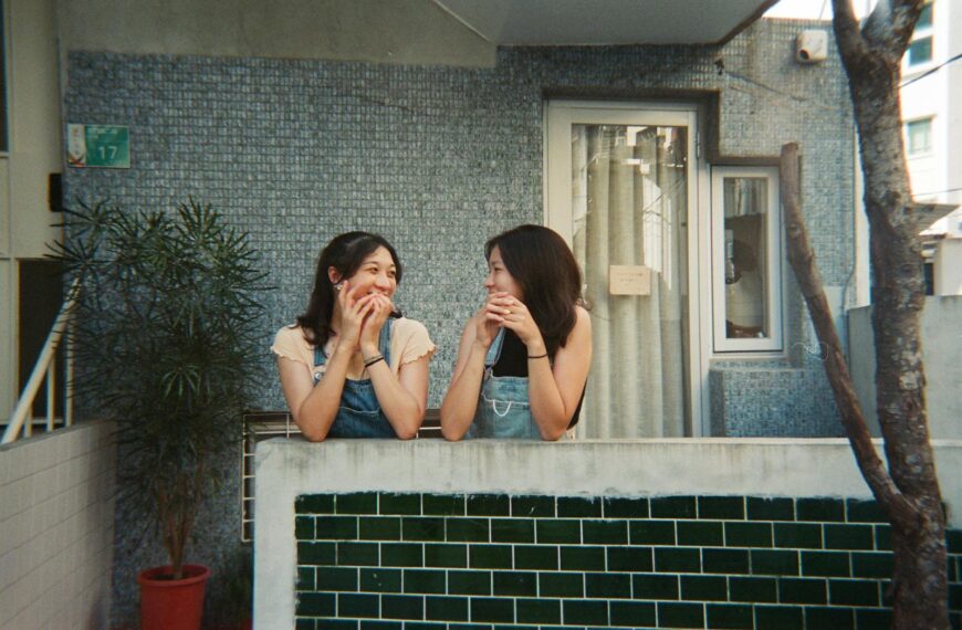 Two women smiling and chatting on a sunny balcony, creating a joyful moment.