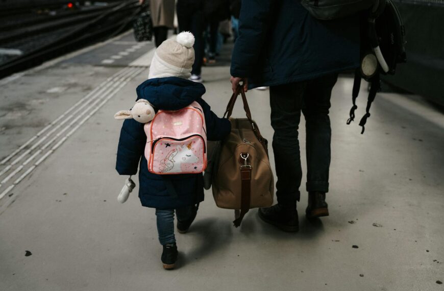 A child and adult carrying bags at a train station platform in Amsterdam.