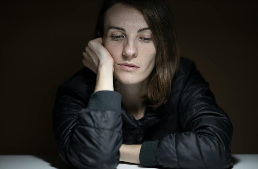 A woman in thought with a serious expression, indoors, in a low-light setting.