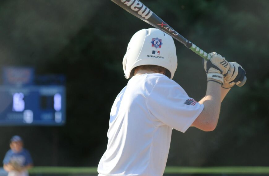 Youth baseball player in white uniform ready to bat during a sunny outdoor game.