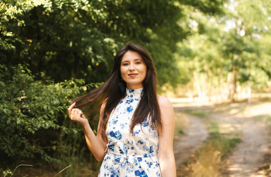 A woman in a blue floral dress enjoys a sunny day in nature, embodying summer bliss.