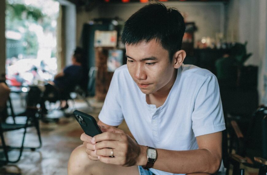 Casually dressed young man engaged with his smartphone, seated indoors.