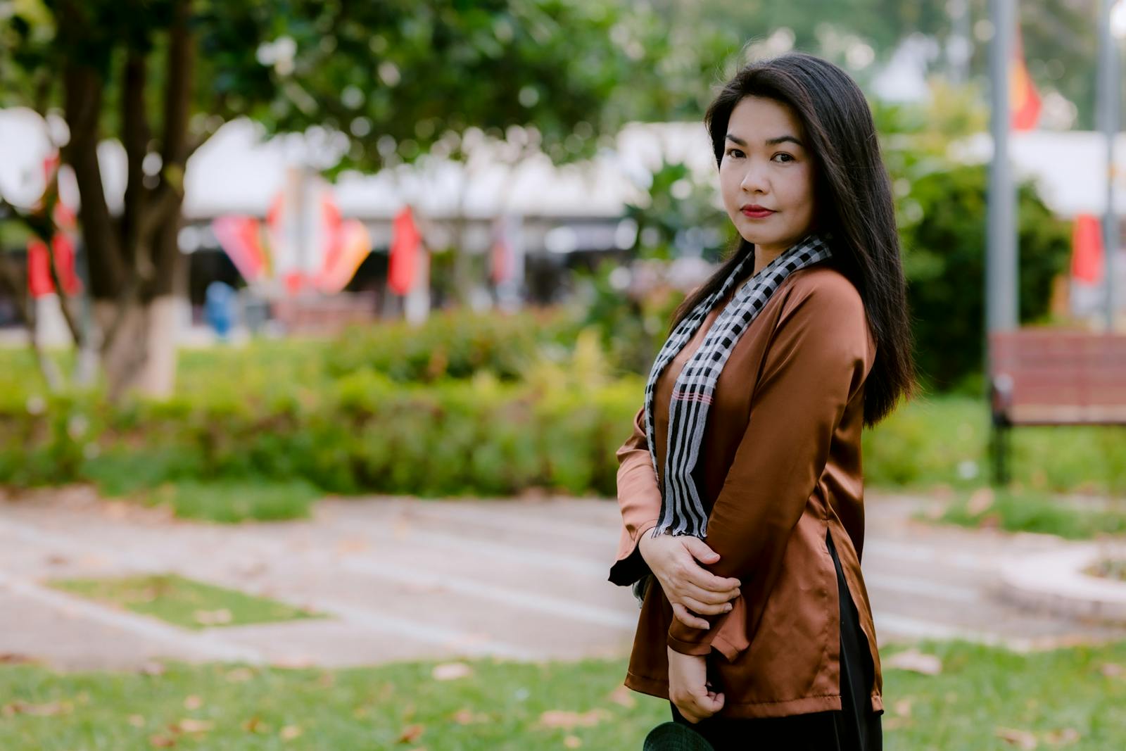 Portrait of a woman standing confidently in an outdoor park setting.