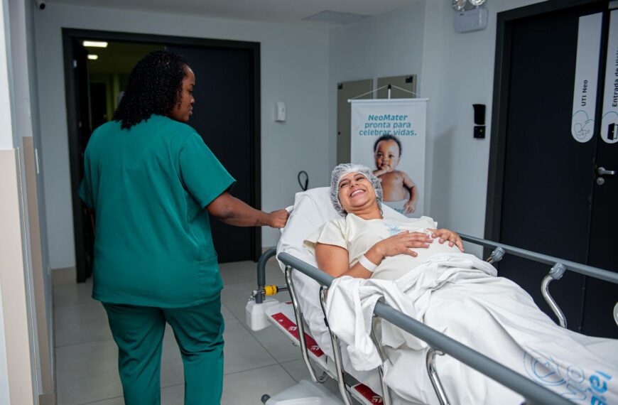 A caring nurse assists a patient in a hospital corridor with a joyful demeanor.