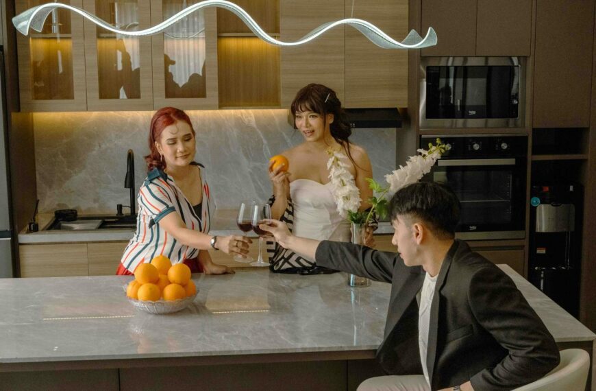 Three friends enjoying drinks and oranges in a stylish kitchen setting.