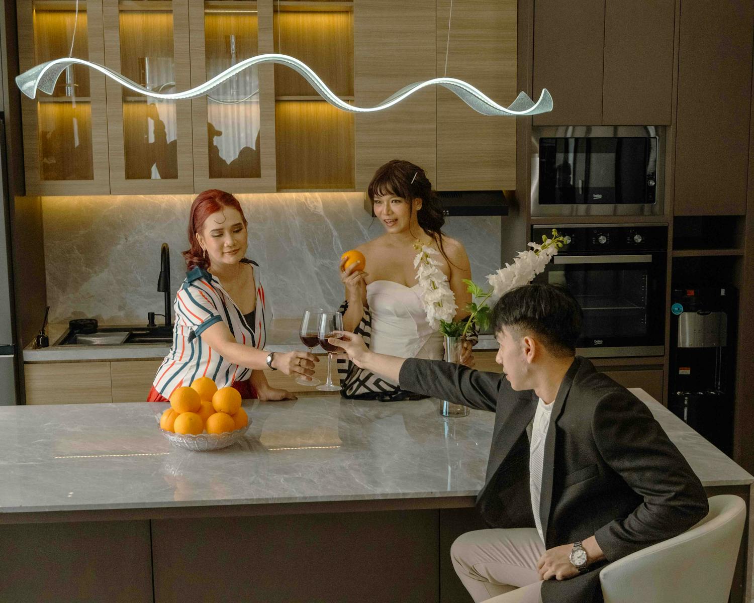 Three friends enjoying drinks and oranges in a stylish kitchen setting.