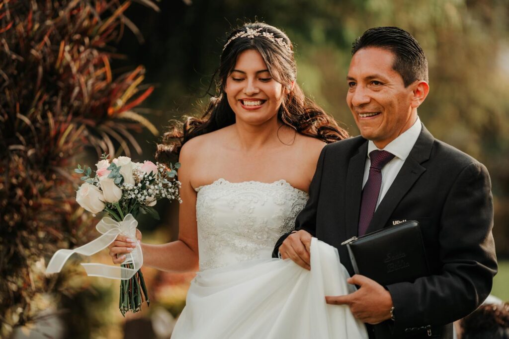 A bride joyfully walks with her father during a wedding ceremony outdoors.