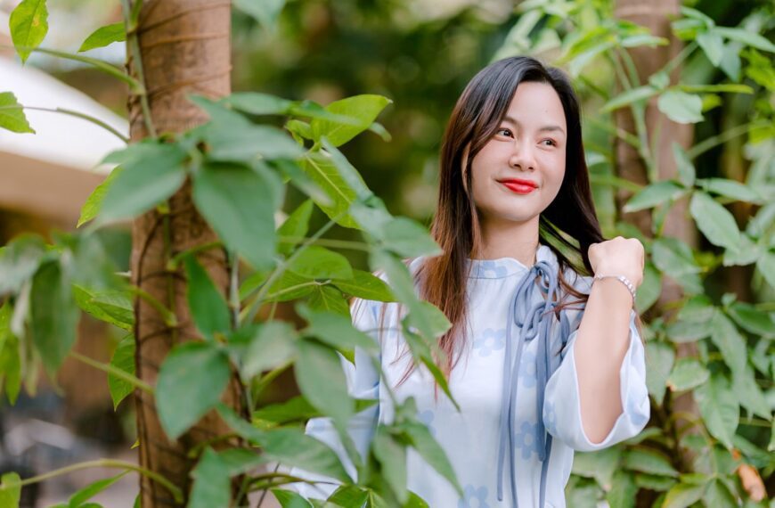Portrait of a smiling woman outdoors amidst lush green foliage, embodying natural beauty.