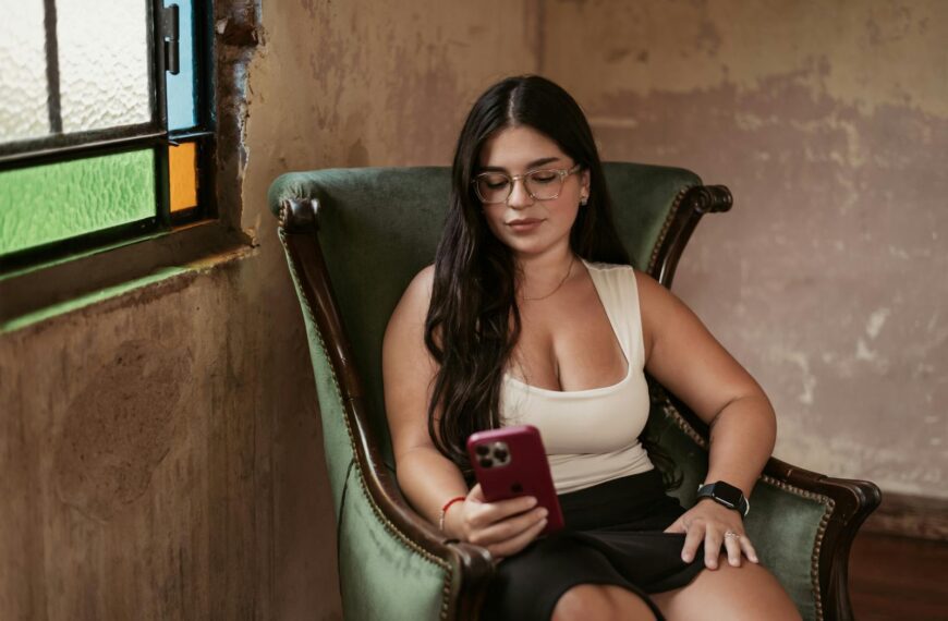 A young woman seated on a chair indoors, using her smartphone, showcasing relaxation and technology.