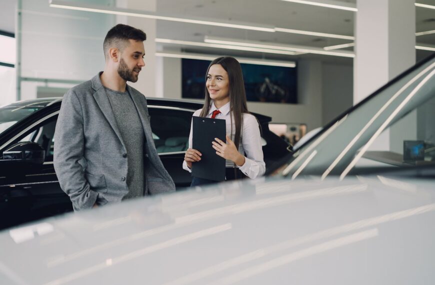 Man consults with salesperson in modern car dealership showroom.