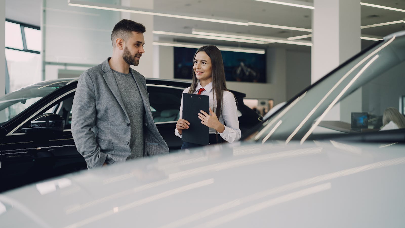 Man consults with salesperson in modern car dealership showroom.