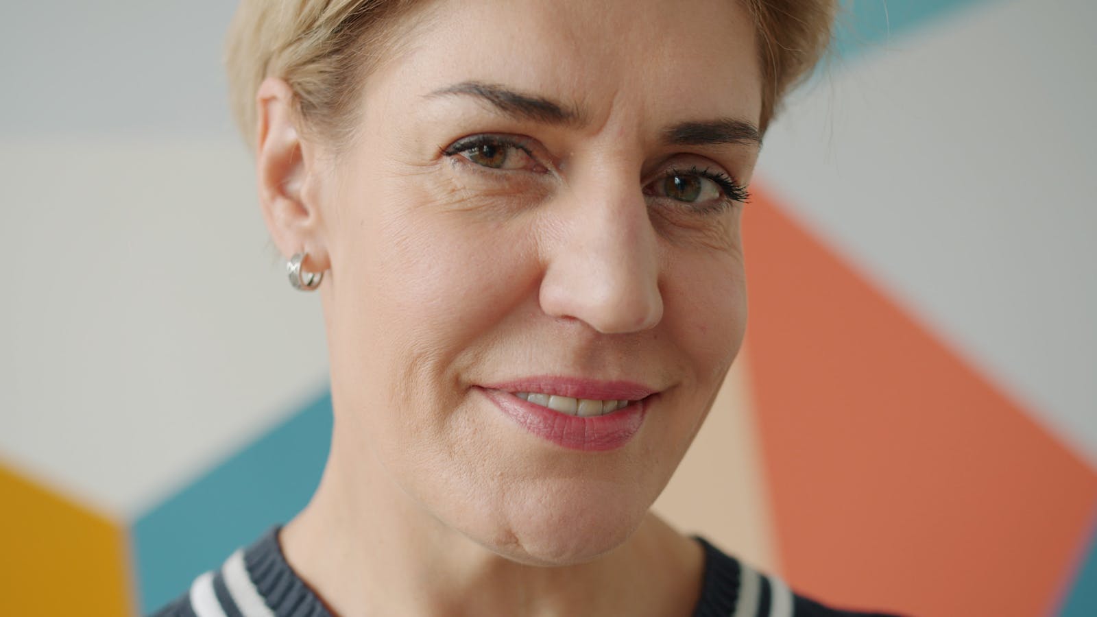 Close-up of a smiling mature woman in front of a colorful geometric background.