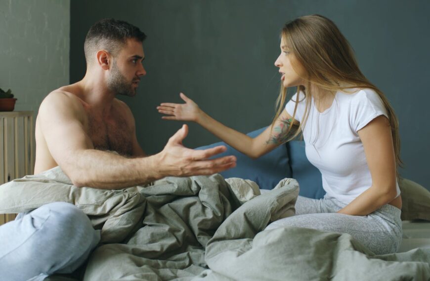 A young couple having a heated argument while sitting on a bed indoors.