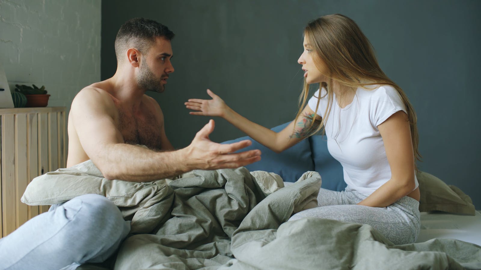 A young couple having a heated argument while sitting on a bed indoors.