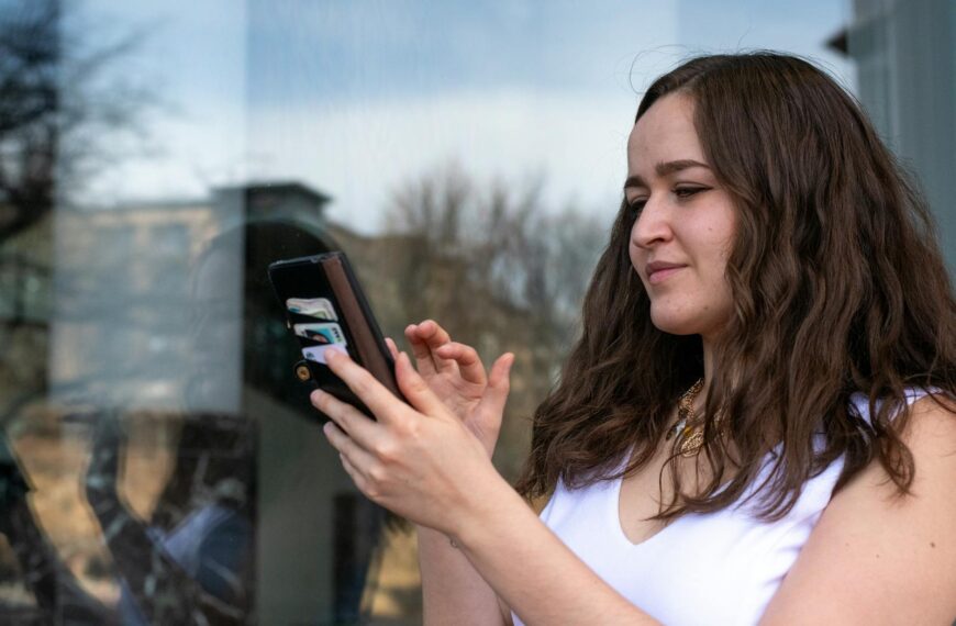 Young woman in a white dress using her smartphone outdoors. Bright day with reflections in a window.
