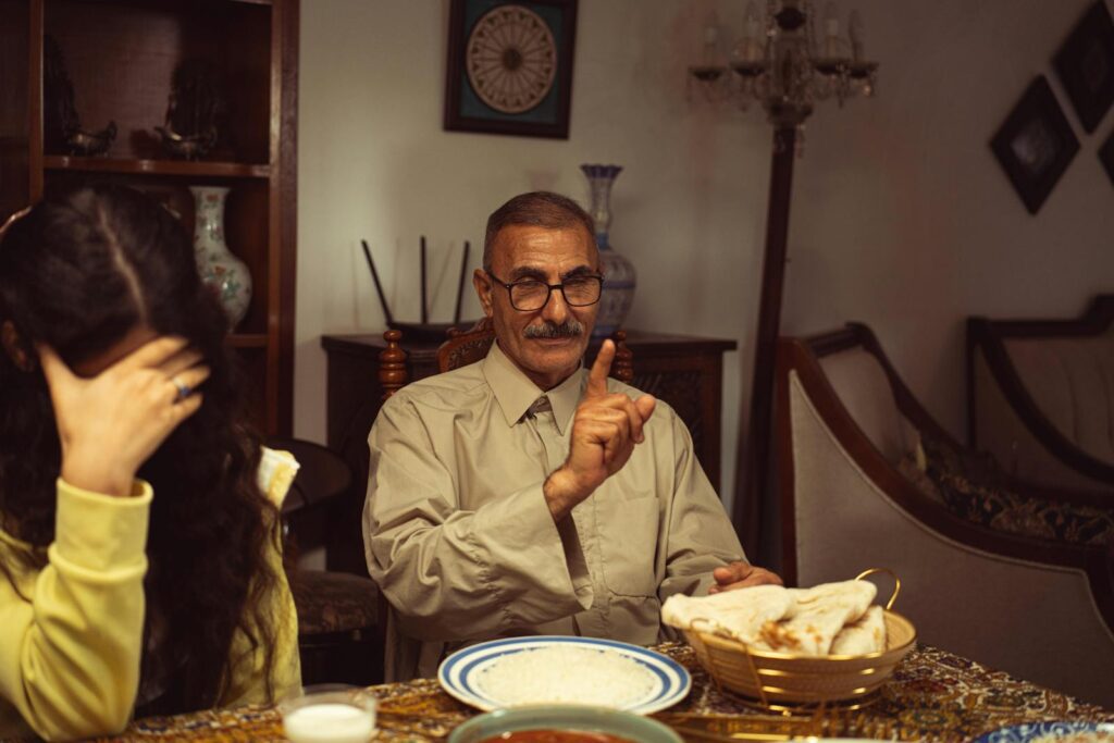 An elder man engages in a serious discussion during family mealtime inside a cozy home setting.