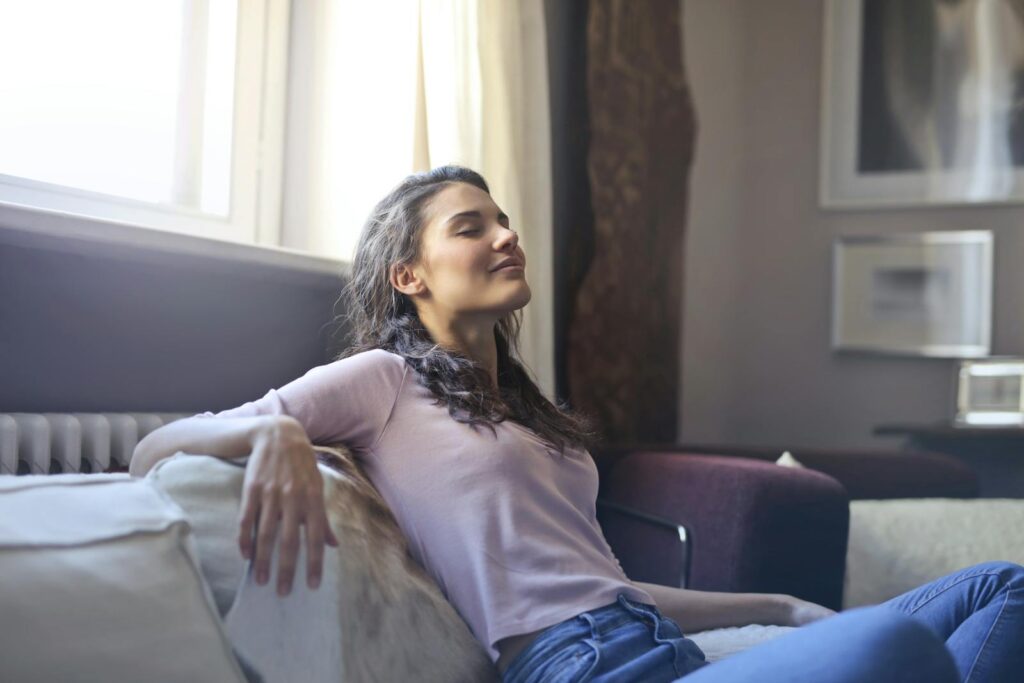 Young woman relaxing on a couch with eyes closed in a cozy living room setting.