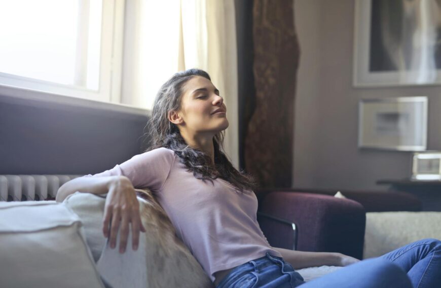 Young woman relaxing on a couch with eyes closed in a cozy living room setting.