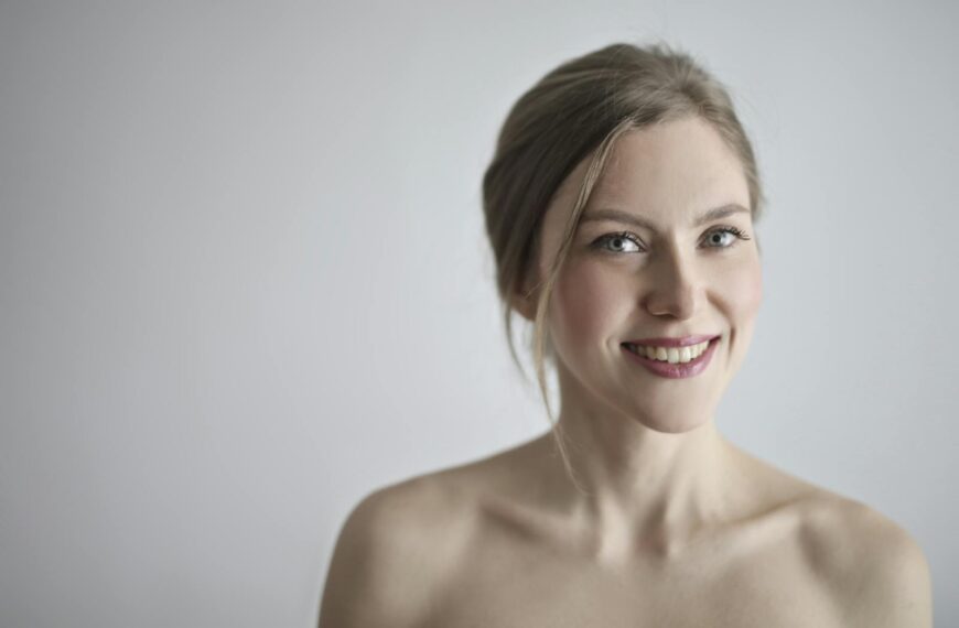 Close-up portrait of a smiling blonde woman against a gray background, embodying elegance and beauty.