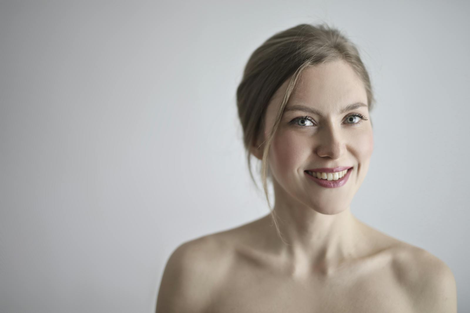 Close-up portrait of a smiling blonde woman against a gray background, embodying elegance and beauty.