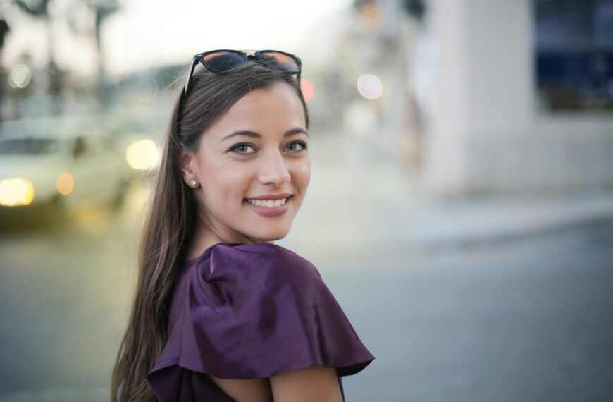 Cheerful woman in a purple top smiles at the camera on a bustling city street.