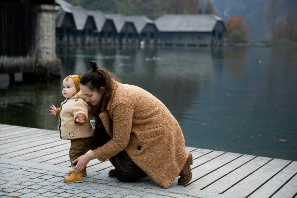 A mother kneels by a lake, assisting her toddler. Scenic autumn setting with wooden docks.