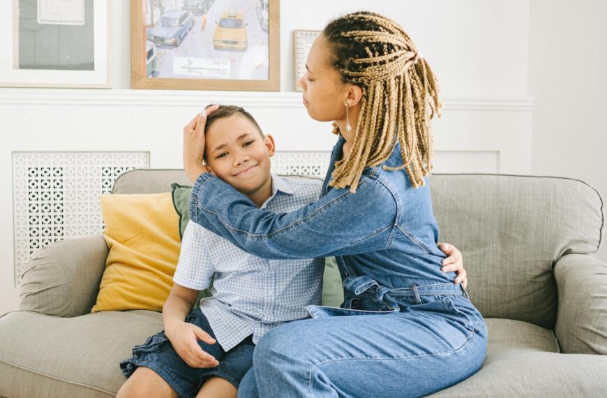 A woman with braids embraces her son on a sofa, creating a warm family moment.