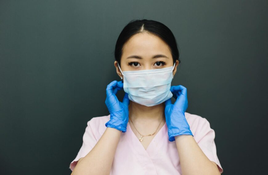 Portrait of a healthcare worker adjusting a face mask, wearing gloves.