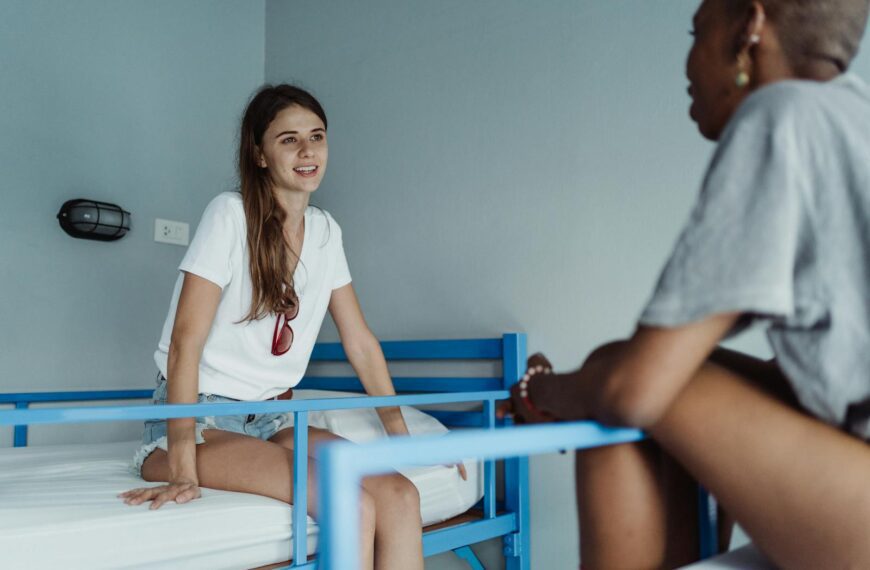 Two women engaged in a friendly conversation in a hostel room with bunk beds.