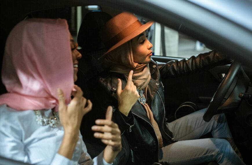 Two women in hijabs enjoy a casual drive in a car, captured from a side view.