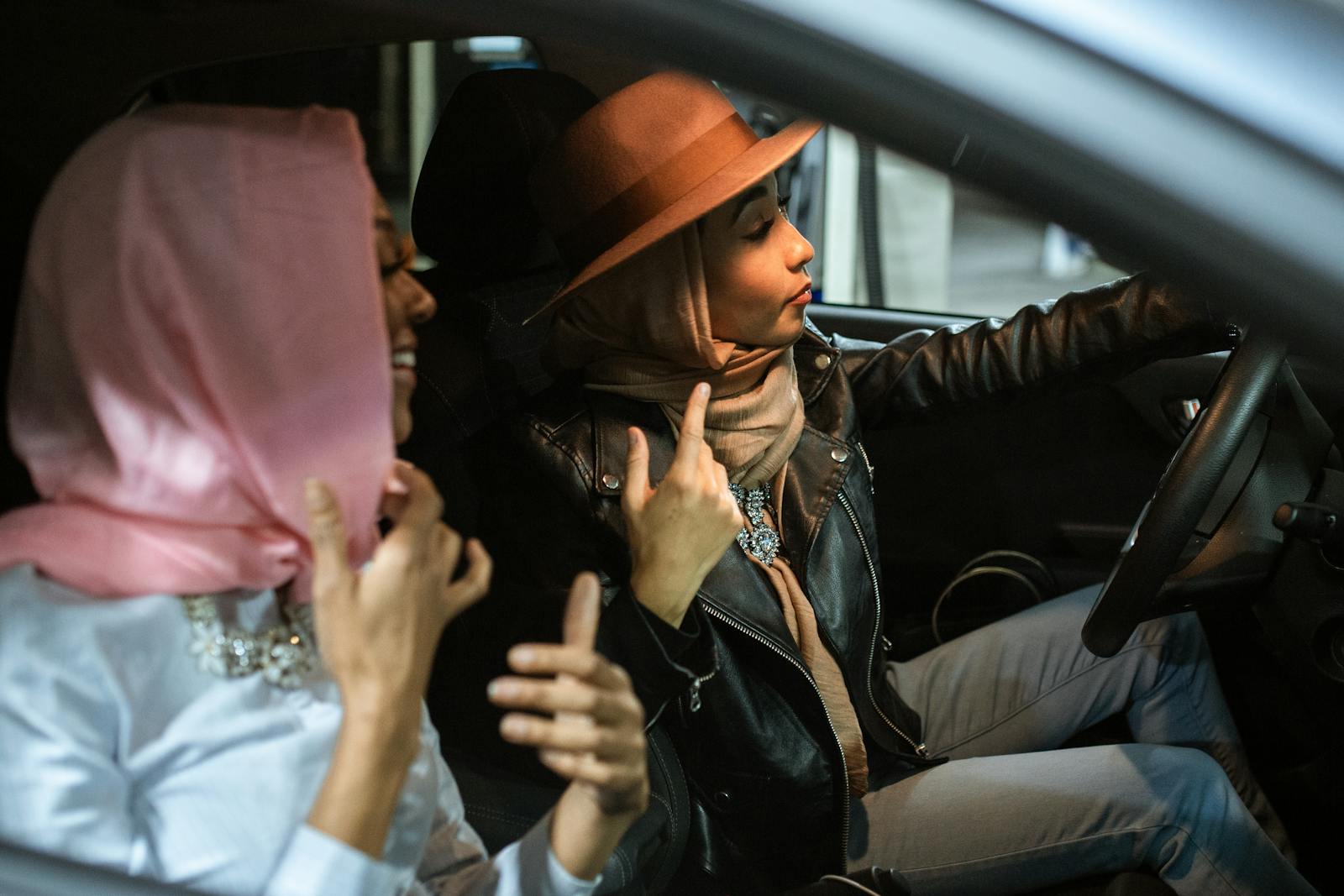 Two women in hijabs enjoy a casual drive in a car, captured from a side view.