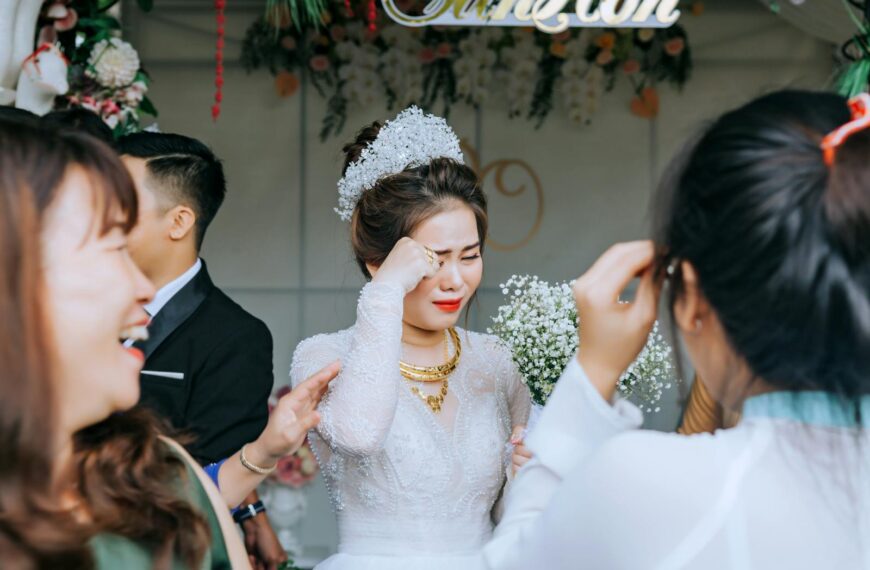 Elegant Asian woman in elegant wedding apparel standing with guests and crying from happiness