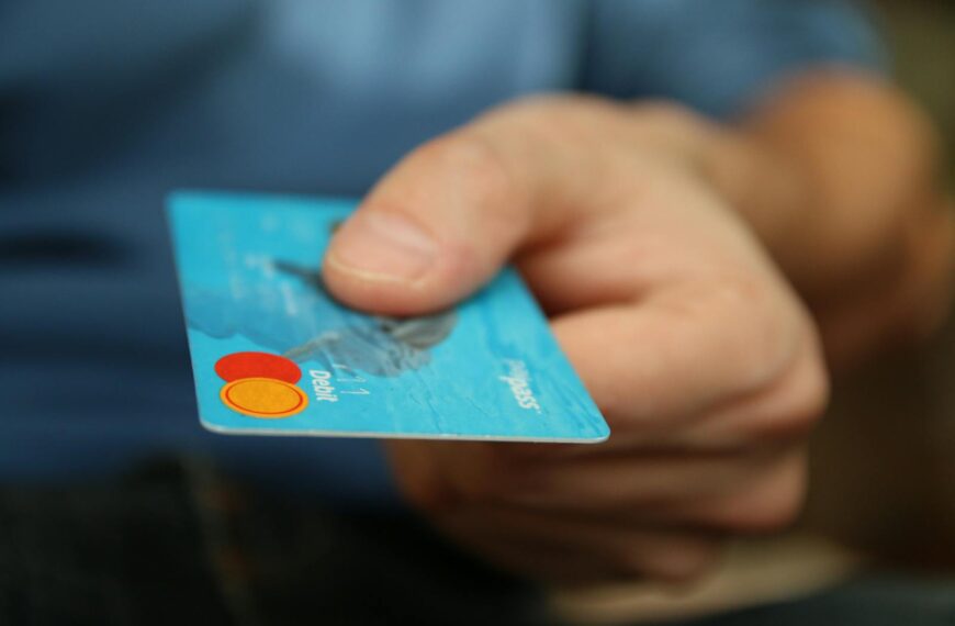 A close-up shot of a hand offering a blue debit card for payment.