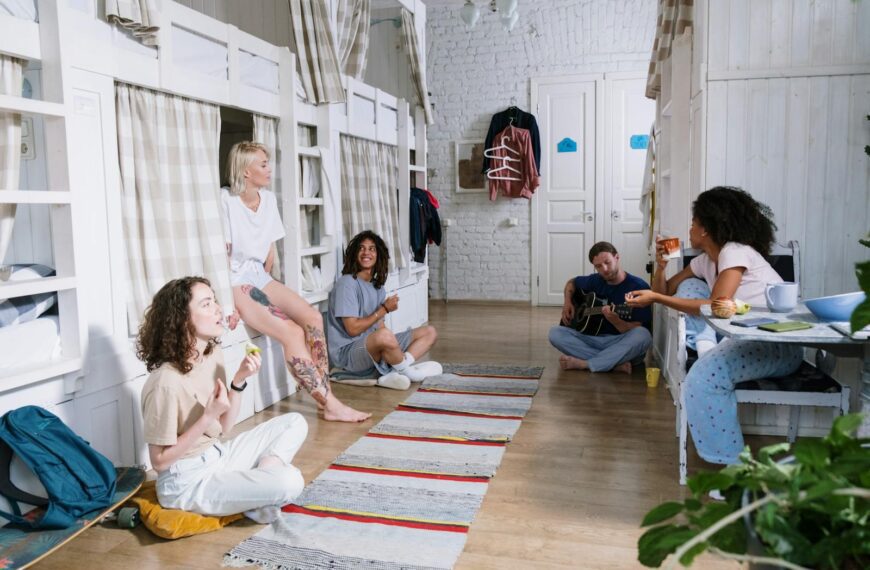 A diverse group of friends enjoying leisure time in a cozy shared dorm room with bunk beds.
