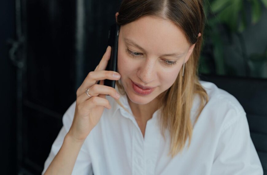 A professional woman in a white shirt making a phone call in an indoor setting, showing communication and business engagement.