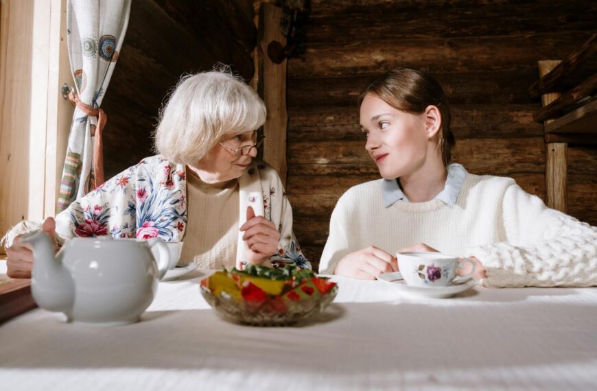 A senior adult and teenager sharing a cozy teatime conversation indoors.