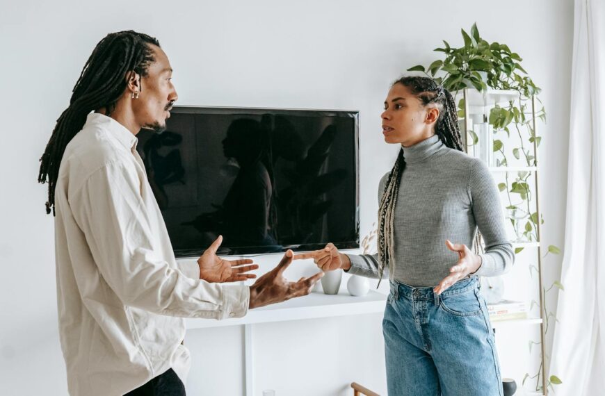 Side view of nervous young African American man and woman with dreadlocks in casual clothes quarreling together in light living room
