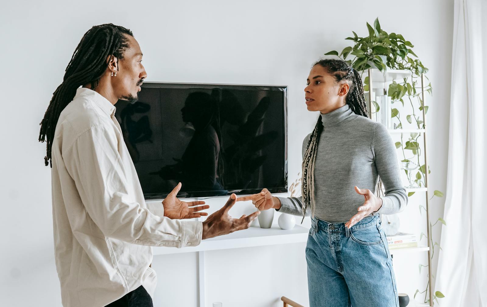 Side view of nervous young African American man and woman with dreadlocks in casual clothes quarreling together in light living room