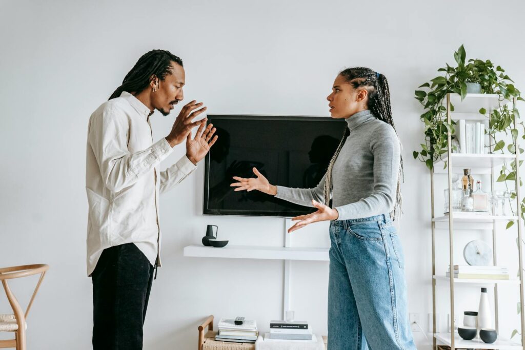 Side view of young African American female in casual outfit gesticulating expressively while arguing with frustrated husband in modern living room