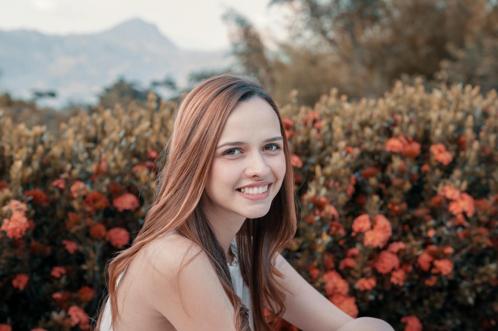 A young woman smiling in front of vibrant orange flowers with mountains in the background.