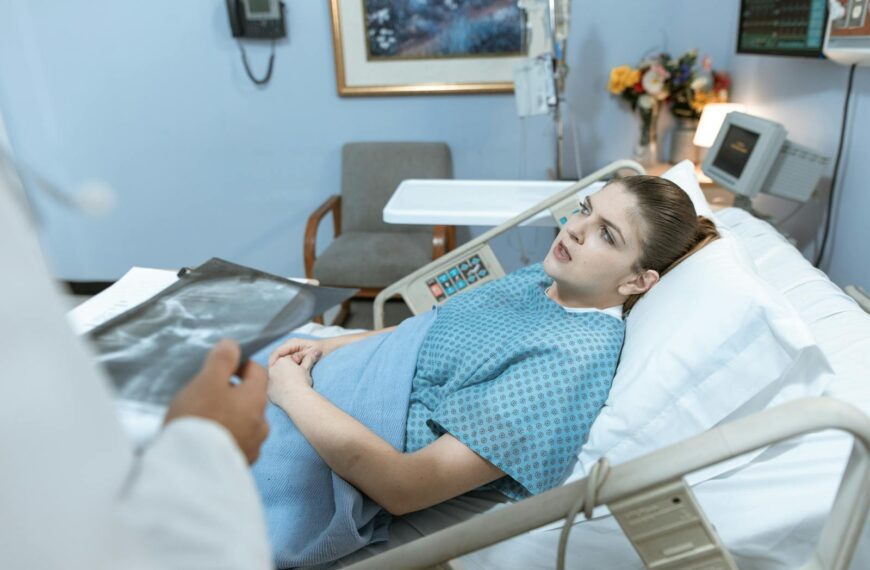 Caucasian woman in hospital bed receiving care from healthcare professional.