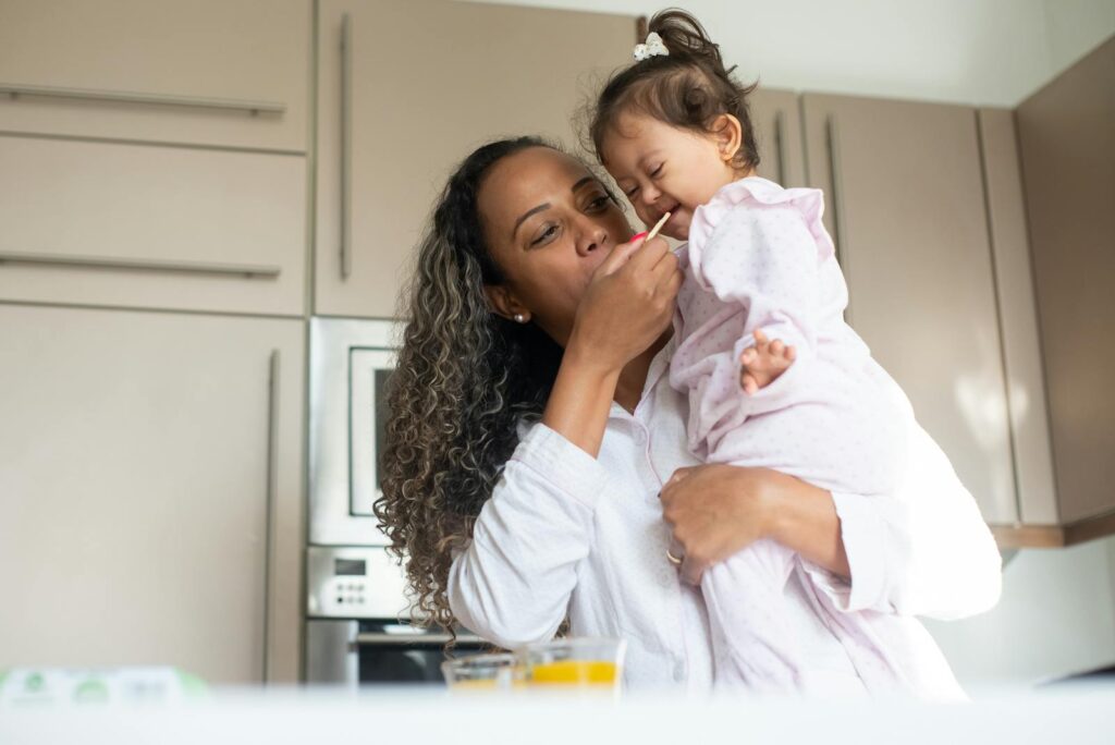 A loving mother feeds her child in a warm kitchen, capturing a moment of tenderness and care.