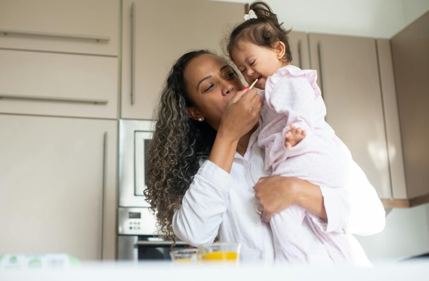A loving mother feeds her child in a warm kitchen, capturing a moment of tenderness and care.