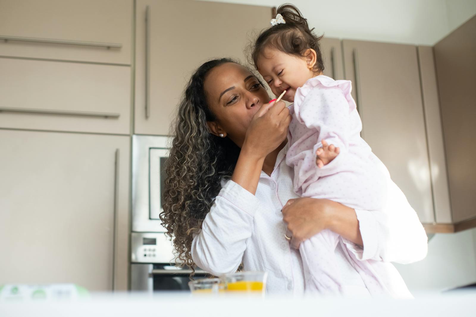 A loving mother feeds her child in a warm kitchen, capturing a moment of tenderness and care.