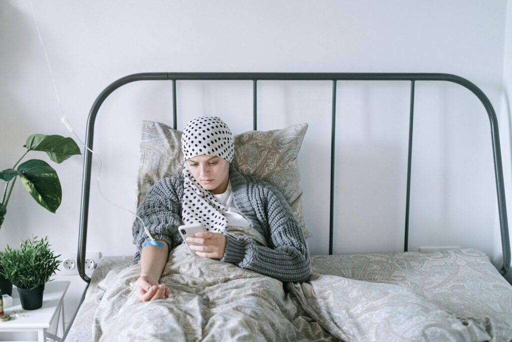 A woman undergoing chemotherapy checks her smartphone in a hospital bed, symbolizing hope and recovery.