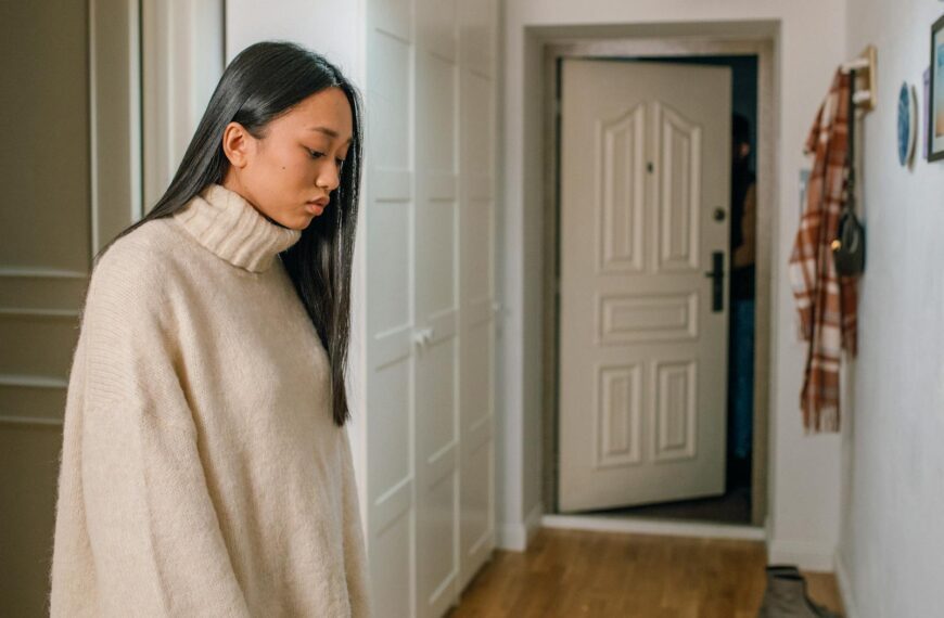 Pensive woman in a turtleneck sweater looking down indoors.